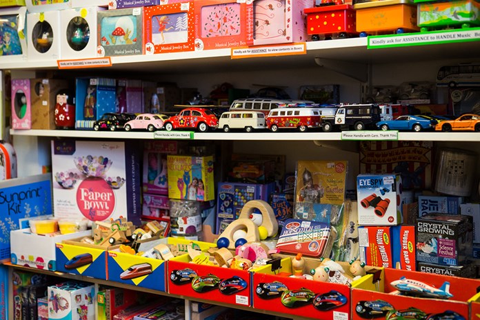 A well-stocked shelf in a toy store displays various children’s toys and games. Model cars, boxes with illustrations, and educational kits are neatly arranged. Wooden animal figures and other educational materials can also be seen. The shelf offers a colorful array of options for young ones to explore and play with.