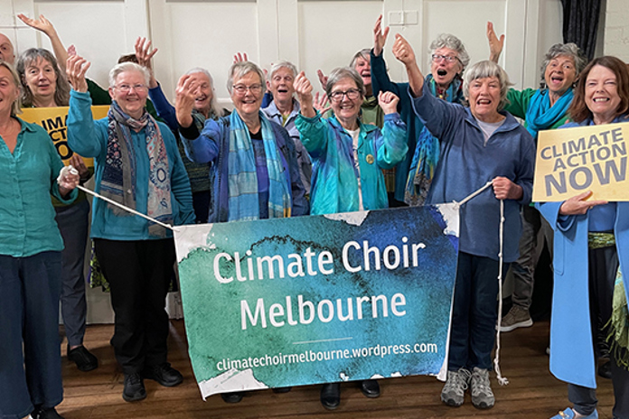 The members of the Climate Choir pose holding a banner for the Climate Choir and one that reads Climate Action Now.