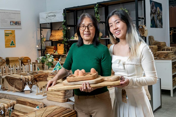 Two people holding a wooden tray with eggs, standing in front of a display of various wooden items at a store.