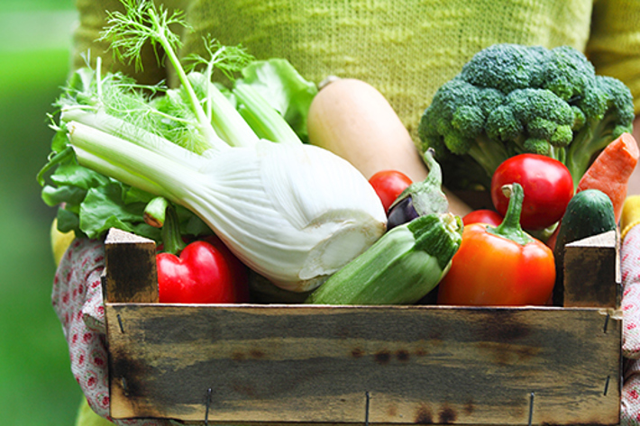 Person holding a wooden box of fresh spring vegetables.